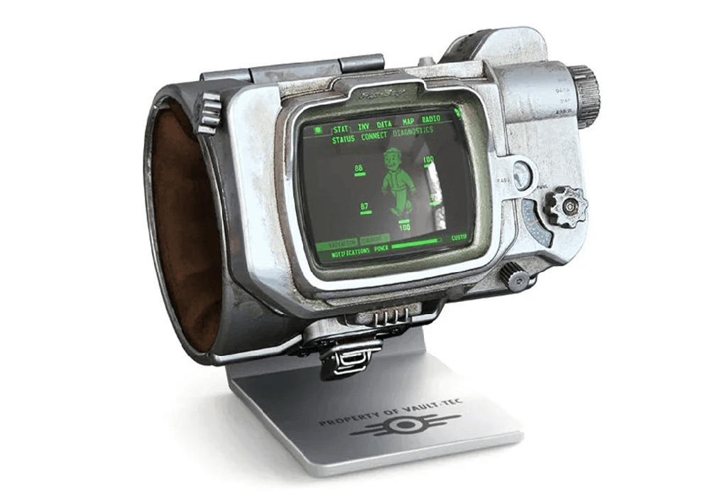 A detailed replica of a Pip-Boy from the Fallout series, featuring a retro-futuristic design with a screen displaying a green monochrome interface. It is mounted on a stand labeled PROPERTY OF VAULT-TEC.