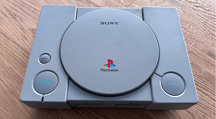 A Playstation 1 conslde on a wooden table top surface.