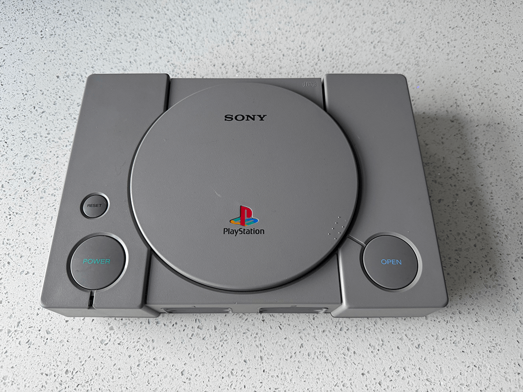 A Playstation 1 conslde on a wooden table top surface.