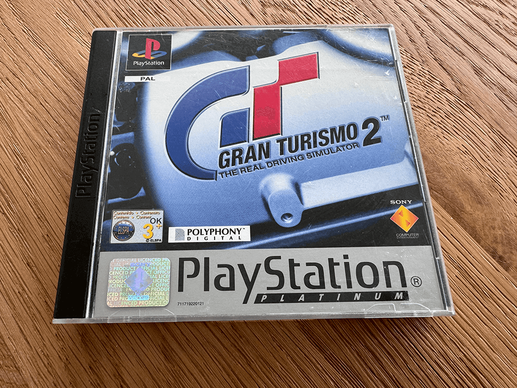 A copy of the Playstation 1 Gran Turismo 2 game in a case in a wooden table top