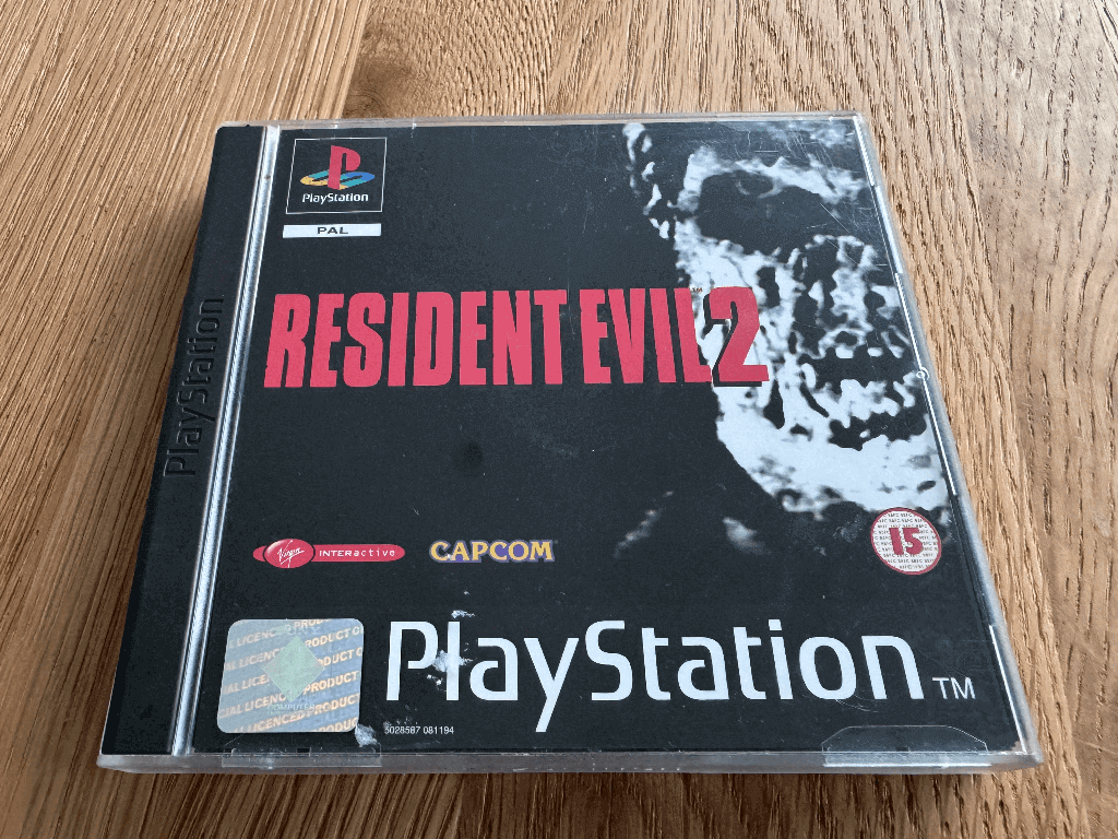 A copy of the Playstation 1 Resident Evil 2 game in a case in a wooden table top.