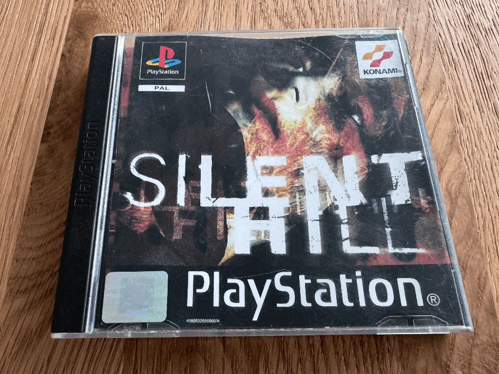 A copy of the Playstation 1 Silent Hill game in a case in a wooden table top.