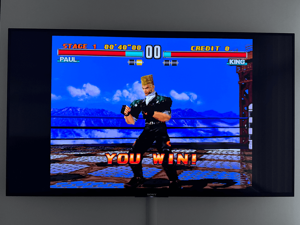 A wall mounted Sony TV dispalying the Tekken 3 game with a character and the words 'You Win'.