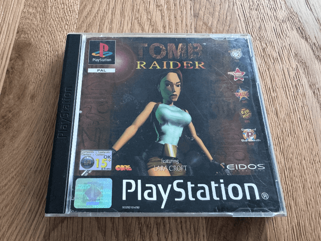 A copy of the Playstation 1 Tomb Raider game in a case in a wooden table top